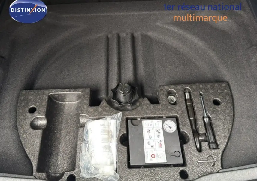 Vue rapprochée du coffre d’un Volkswagen Touran blanc 2018 montrant le kit de réparation pneu et outils intégrés.