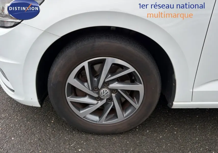 Gros plan sur la roue avant gauche d’un Volkswagen Touran blanc avec jante alliage gris foncé.
