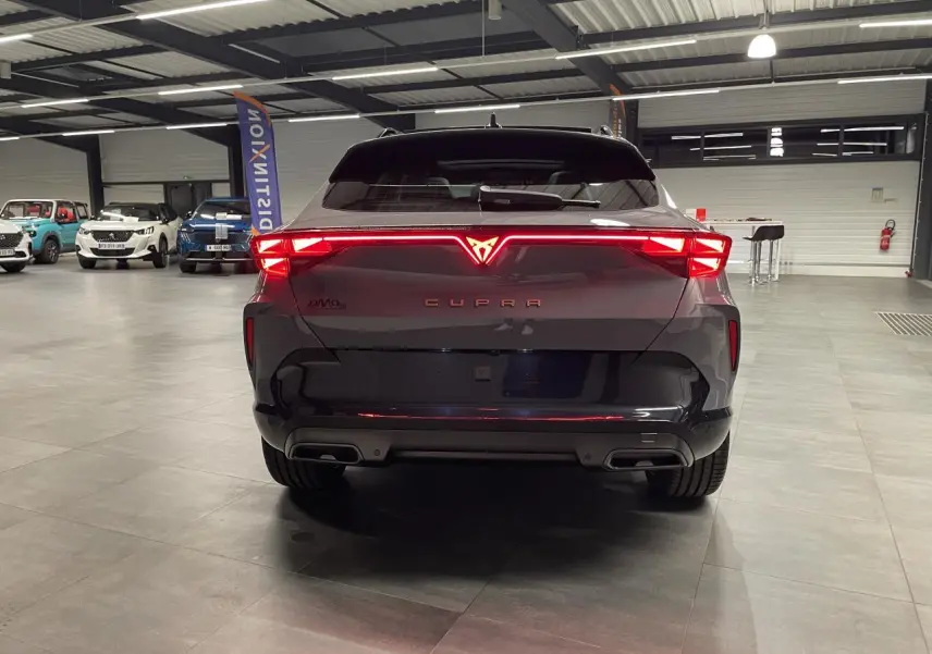 Vue arrière d'une CUPRA Formentor gris Graphene avec feux arrière Tri-LED allumés et double sortie d'échappement noire.