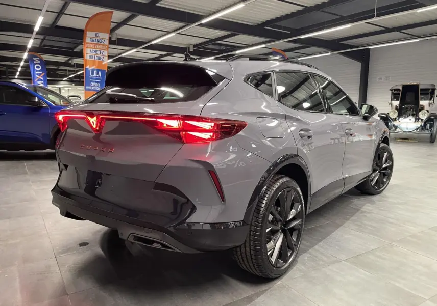 Vue 3/4 arrière droite du CUPRA Formentor gris Graphene avec feux arrière allumés et jantes alliage noires en showroom.