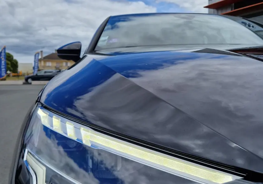 Gros plan sur le phare avant gauche LED d'une Audi A3 Sportback noire, reflétant un ciel nuageux.