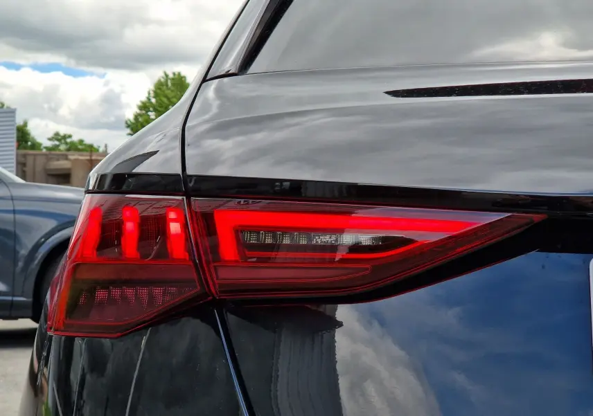 Gros plan sur le feu arrière droit rouge d'une Audi A3 Sportback noire, reflet du ciel nuageux sur la carrosserie.