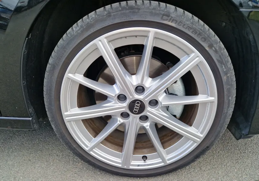Gros plan sur la roue avant gauche d’une Audi A3 Sportback noire, jante alliage argentée Audi Sport visible.