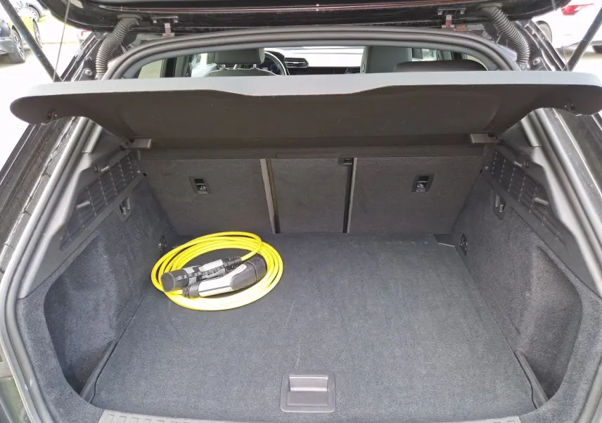 Coffre ouvert vu de l'arrière d'une Audi A3 Sportback noire avec câble de recharge jaune visible à l'intérieur.