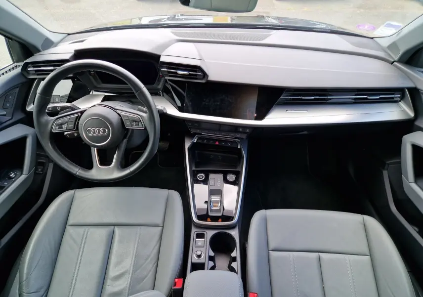 Vue intérieure avant de l'Audi A3 Sportback 40 TFSI-e 2021, tableau de bord moderne avec volant multifonction noir et sièges cuir gris.