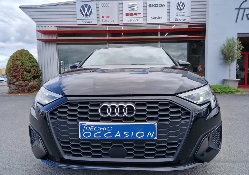 Vue frontale d'une Audi A3 Sportback noire 2021 avec calandre hexagonale et logo Audi visible, stationnée devant un garage.