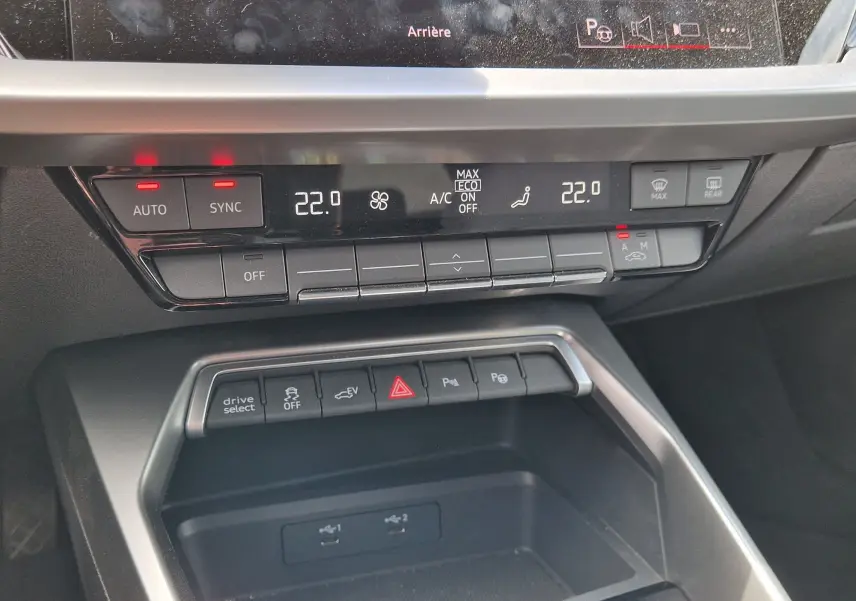 Vue rapprochée du tableau de bord noir de l'Audi A3 Sportback 40 TFSI-e 2021, montrant les commandes climatisation et boutons fonctionnels.