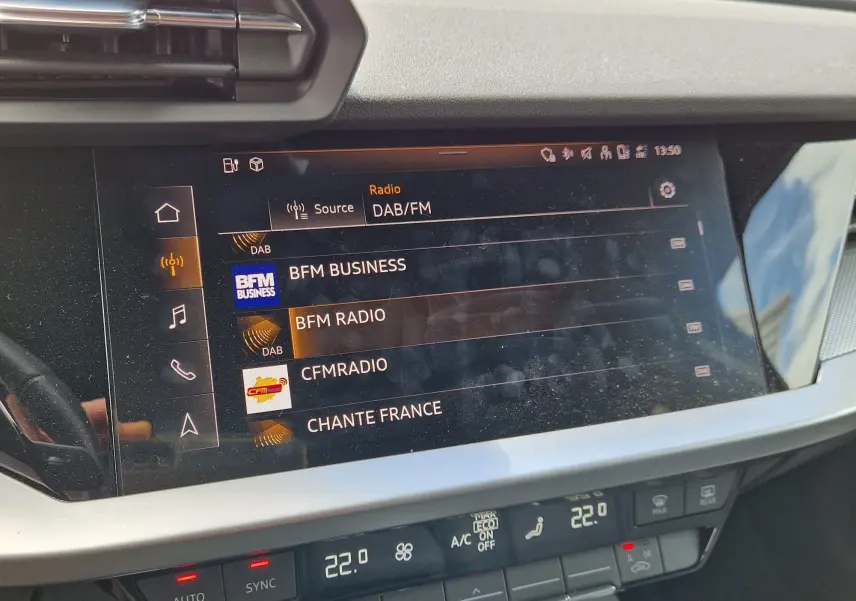 Vue rapprochée de l’écran tactile central de l’Audi A3 Sportback noir 2021, affichant les stations radio DAB/FM.