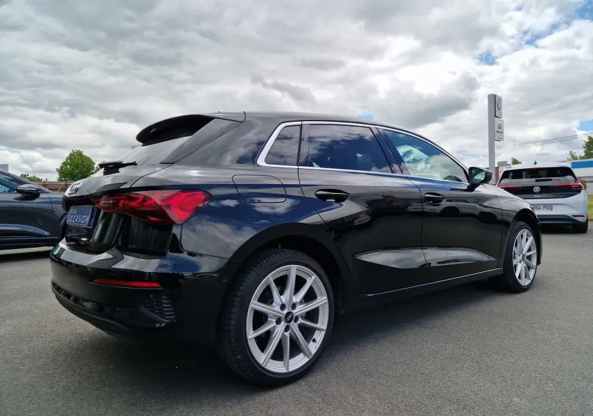 Audi A3 Sportback noir vue 3/4 arrière droit, jantes alliage argent et vitres teintées sous ciel nuageux.