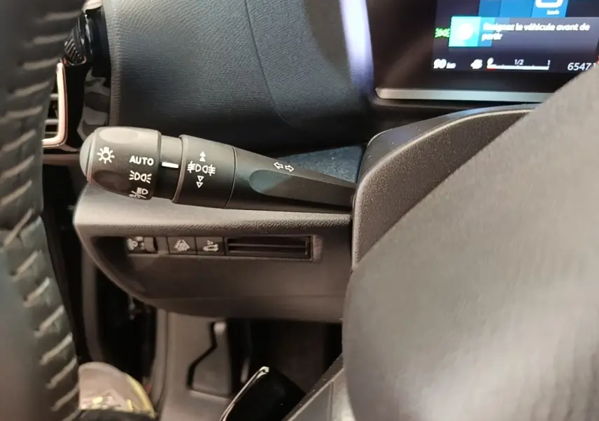 Gros plan sur la manette de commande des phares et clignotants à gauche du volant dans l’habitacle noir du Citroën C4 X.