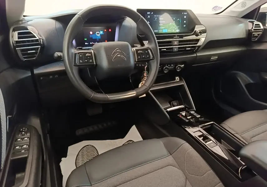 Intérieur de la Citroën C4 X noir, vue du poste de conduite avec volant cuir multifonctions et écran tactile central.