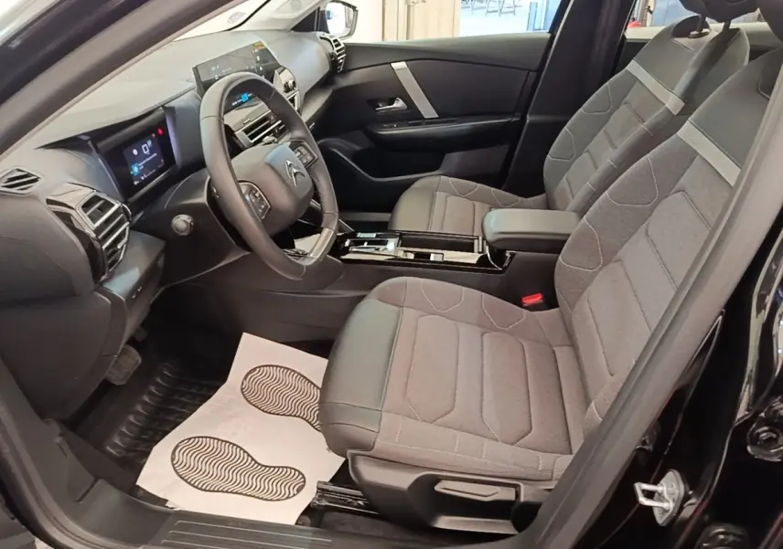 Intérieur avant droit d'une Citroën C4 X noire 2023, sièges tissu gris et volant cuir multifonctions.