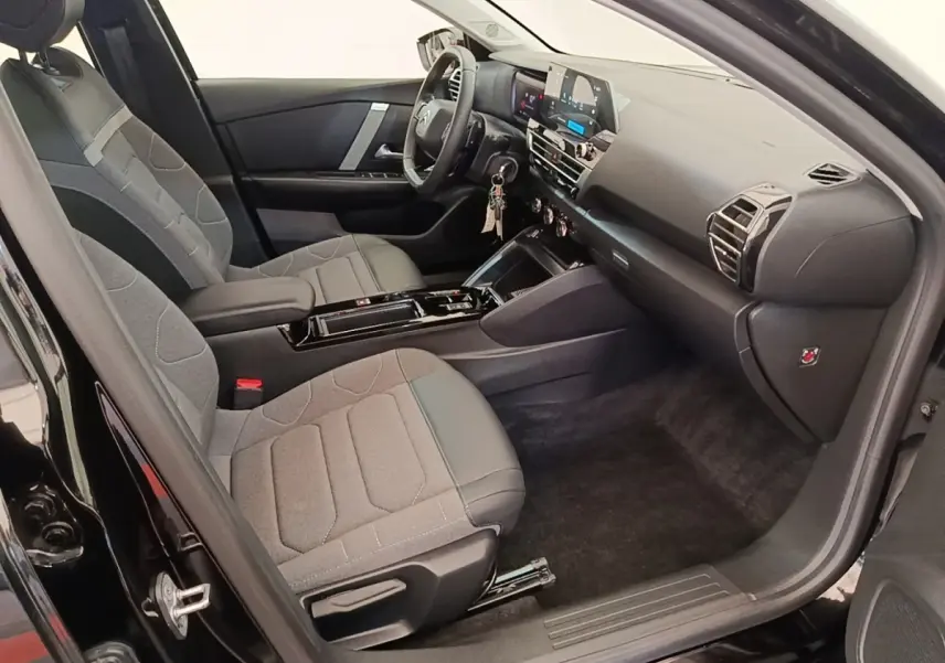 Vue intérieure côté conducteur de la Citroën C4 X noire 2023, sièges tissu gris et tableau de bord moderne.