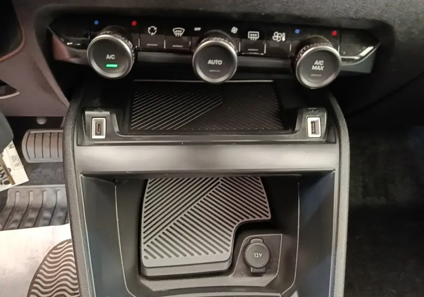 Vue rapprochée de la console centrale noire de la Citroën C4 X avec commandes climatisation et prises USB et 12V visibles.