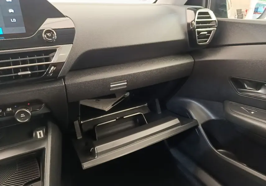 Intérieur noir de la Citroën C4 X 2023, vue côté passager avec boîte à gants ouverte et tableau de bord visible.