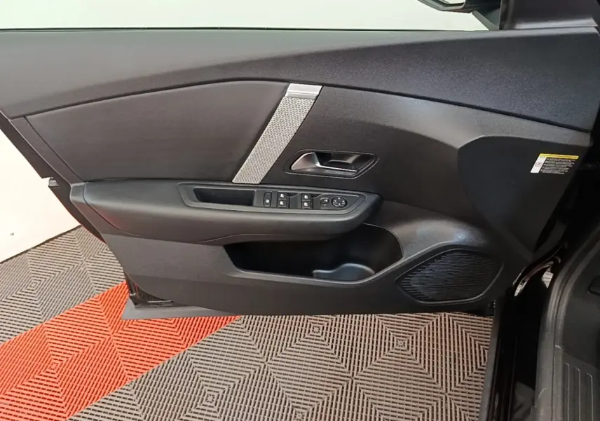 Vue intérieure côté gauche de la porte avant noire de la Citroën C4 X avec commandes de vitres et haut-parleur intégré.