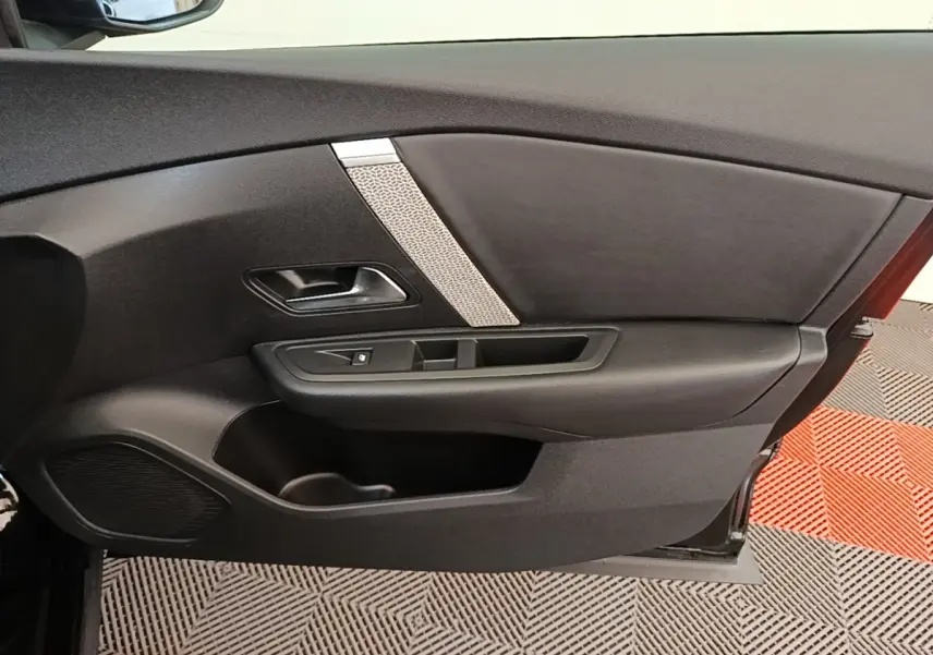 Vue intérieure du panneau de porte avant gauche noir de la Citroën C4 X 2023 avec poignée et commande de vitre.