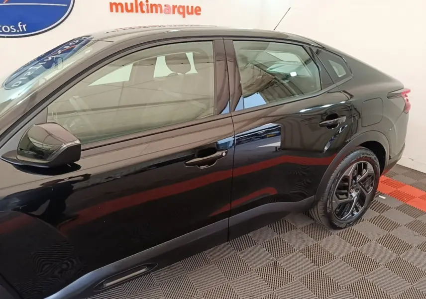Vue latérale droite d'une Citroën C4 X noire 2023 avec jantes noires et lignes fluides sur fond intérieur.