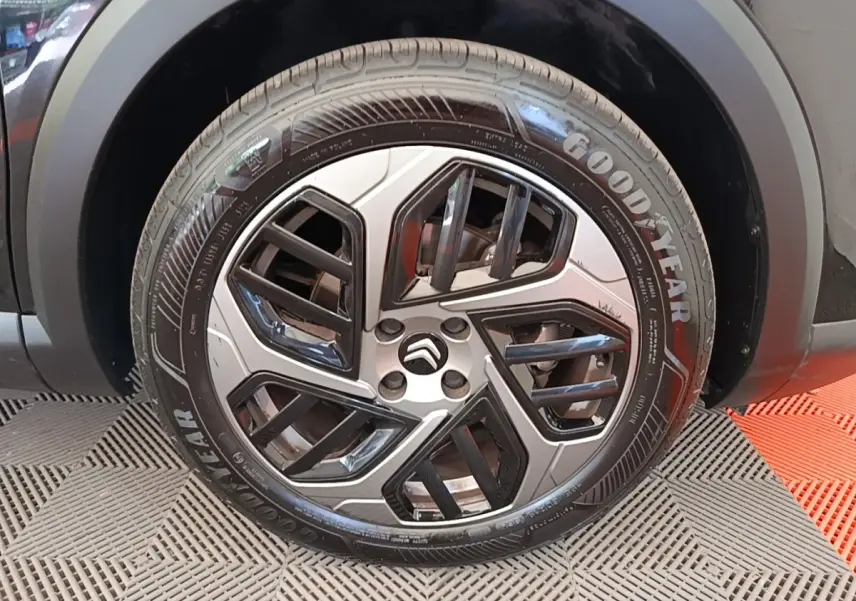 Gros plan sur la roue avant droite d'une Citroën C4 X noire, jante alliage au design géométrique bicolore.