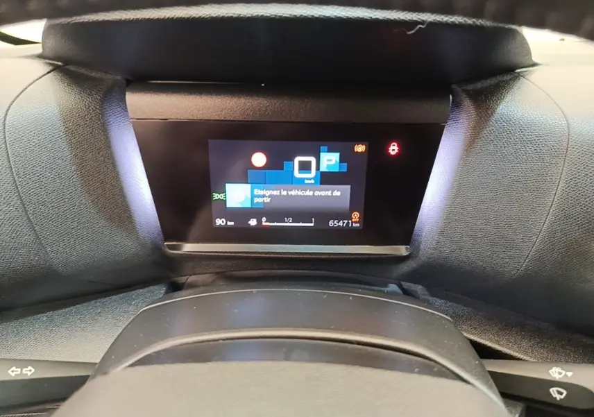 Vue rapprochée du tableau de bord numérique de la Citroën C4 X noire, affichant un message d'alerte au stationnement.