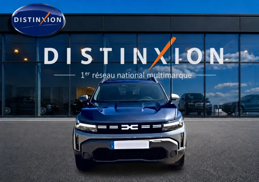 Vue avant d'un Dacia Duster gris schiste 2026 avec calandre lumineuse, devant une vitrine Distinxion.