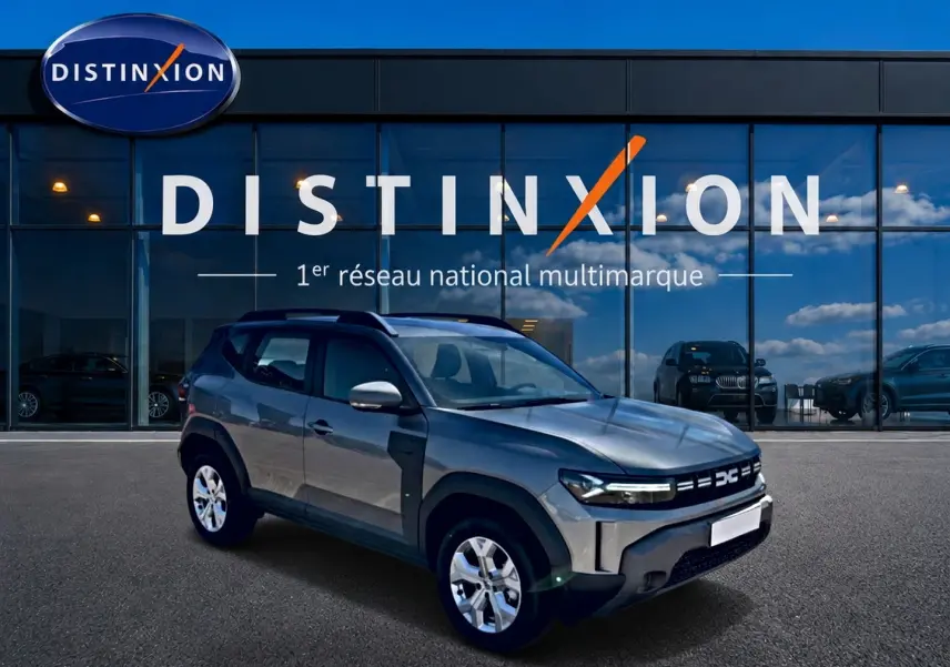 Dacia Duster gris schiste en 3/4 avant droit, avec jantes alu et rétroviseurs argentés devant showroom Distinxion.