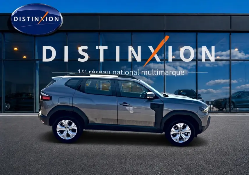 Profil droit du Dacia Duster gris schiste 2026 devant une vitrine avec logo Distinxion.