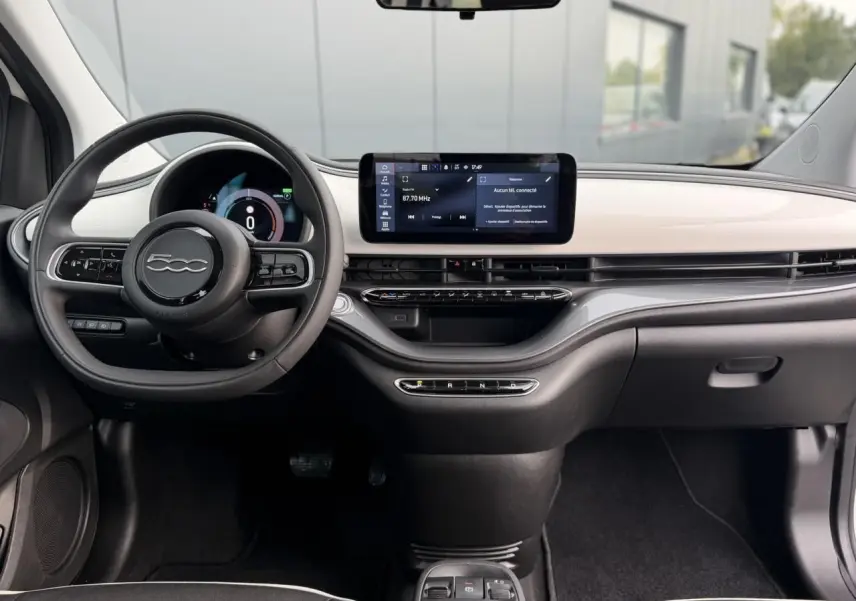Vue intérieure frontale du tableau de bord blanc et noir de la Fiat 500 électrique 2024 avec écran tactile et volant multifonction.
