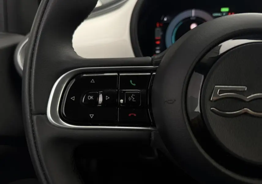 Gros plan sur la partie gauche du volant noir de la FIAT 500 électrique blanche avec commandes intégrées.