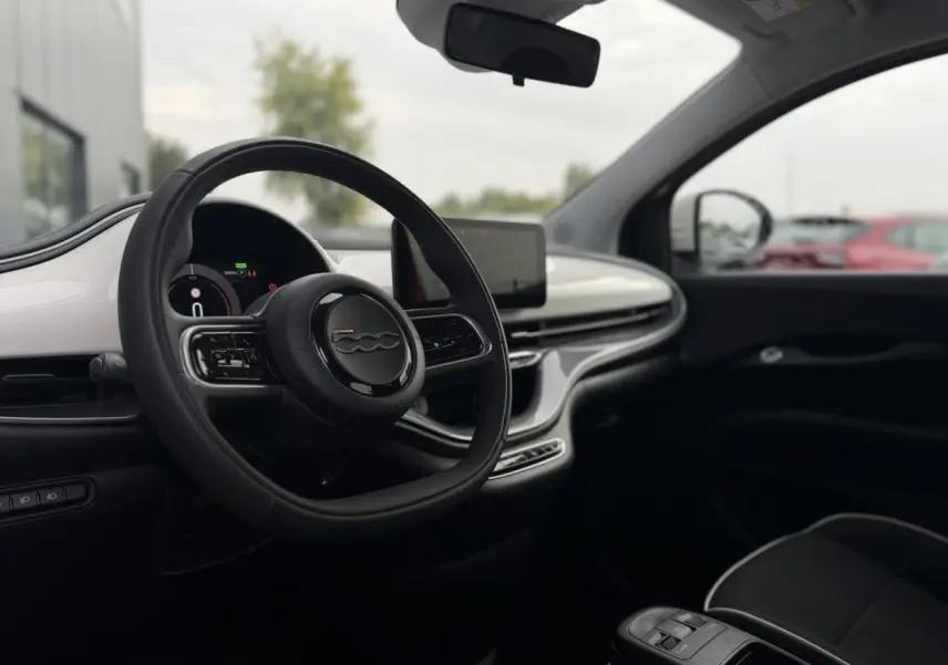 Intérieur de la Fiat 500 électrique 2024 vue côté conducteur, tableau de bord blanc et volant noir avec logo 500.
