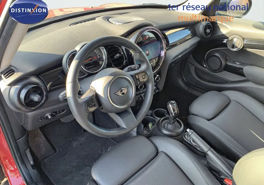 Intérieur avant droit d'une MINI rouge chili 2023 avec tableau de bord moderne et sièges cuir noir.
