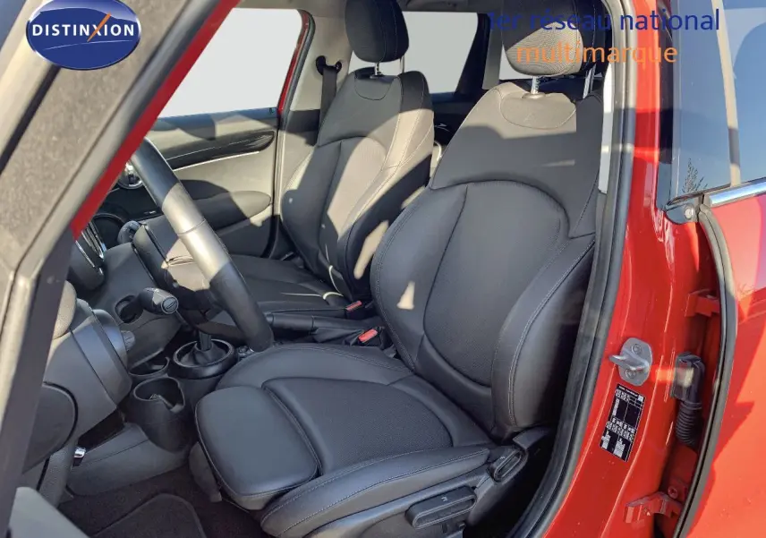 Vue intérieure côté conducteur d'une MINI rouge chili 2023 avec sièges avant en cuir noir et volant visible.