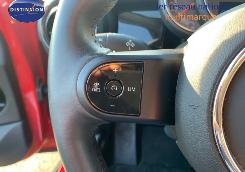 Gros plan sur le volant de la MINI 2023 rouge chili, montrant les commandes de régulateur de vitesse à gauche.