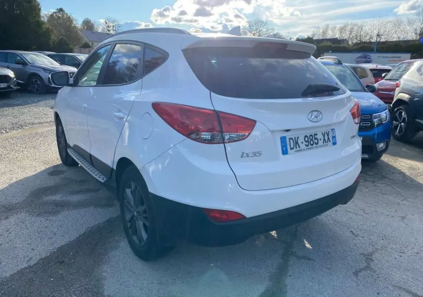 Vue 3/4 arrière droite d'un Hyundai ix35 blanc avec vitres teintées et jantes foncées sur un parking.
