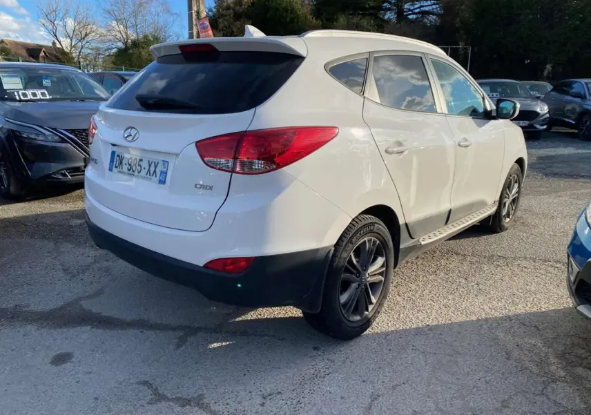 Hyundai ix35 blanc vu en 3/4 arrière droit, avec jantes alliage et vitres teintées sur parking extérieur.
