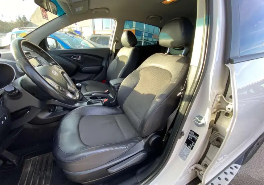 Intérieur avant droit du Hyundai ix35 blanc 2014, sièges tissu-cuir et volant avec commandes intégrées.