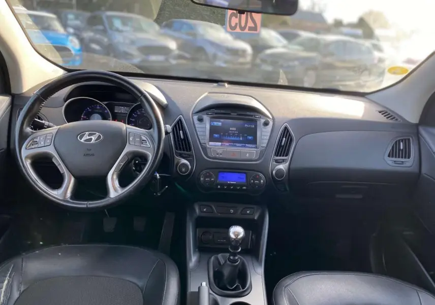 Intérieur du Hyundai ix35 blanc 2014, vue frontale du tableau de bord avec volant, écran tactile et levier de vitesse manuel.