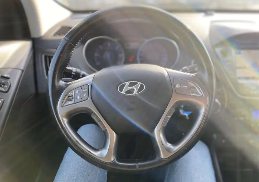 Volant cuir du Hyundai ix35 2014 vu de face, avec commandes intégrées et tableau de bord flou en arrière-plan.
