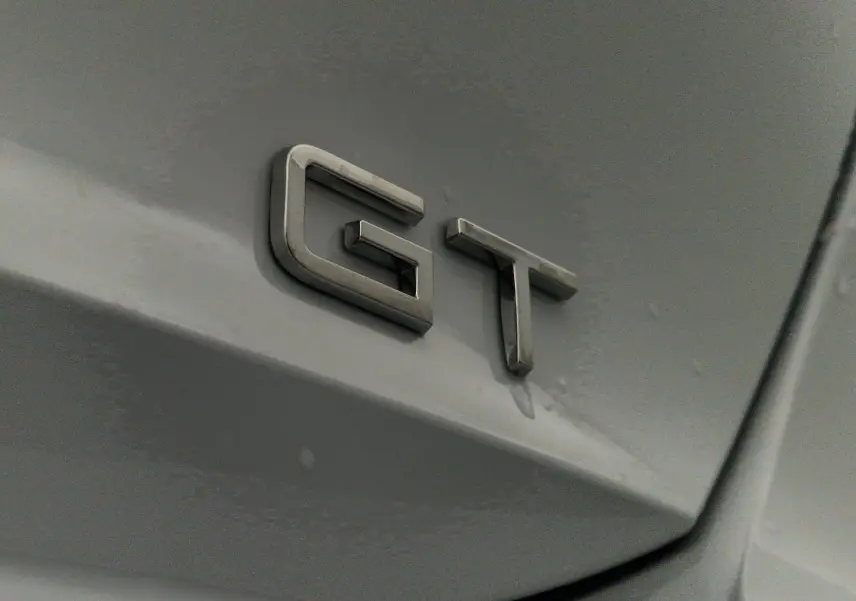 Gros plan sur l'emblème GT en métal sur la carrosserie blanche Okenite d'une Peugeot 308 2025.