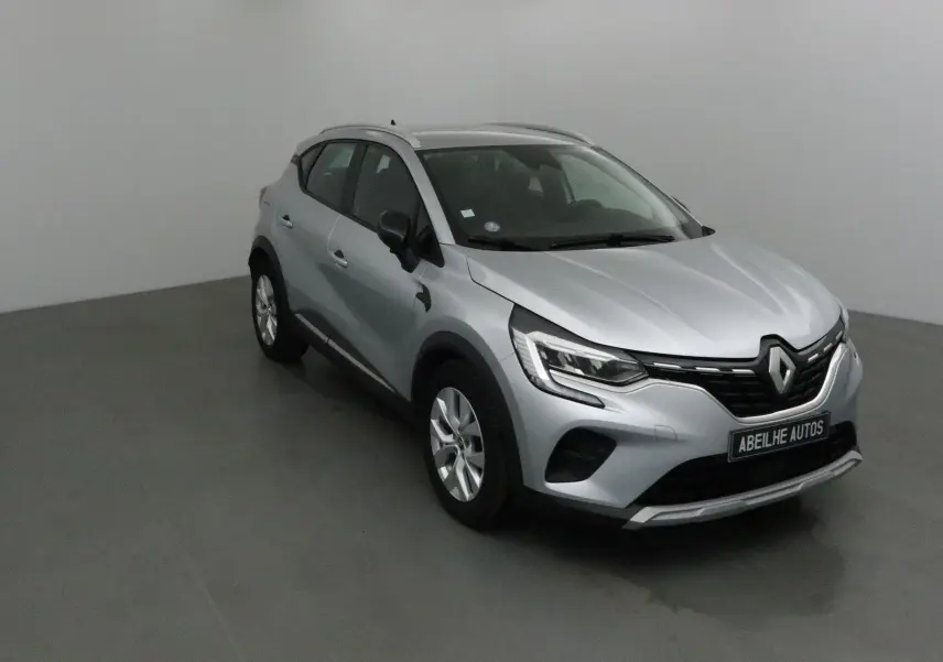 Renault Captur gris Highland en 3/4 avant droit, mettant en valeur ses optiques LED et sa calandre noire distinctive.