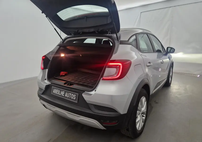Vue 3/4 arrière droite d’un Renault Captur gris Highland 2020 avec coffre ouvert et feux arrière allumés.