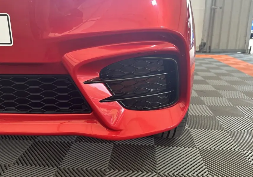 Gros plan sur la partie avant droite rouge de l'AIXAM AMBITION 0.5 CITY SPORT avec grille noire et détails sportifs.