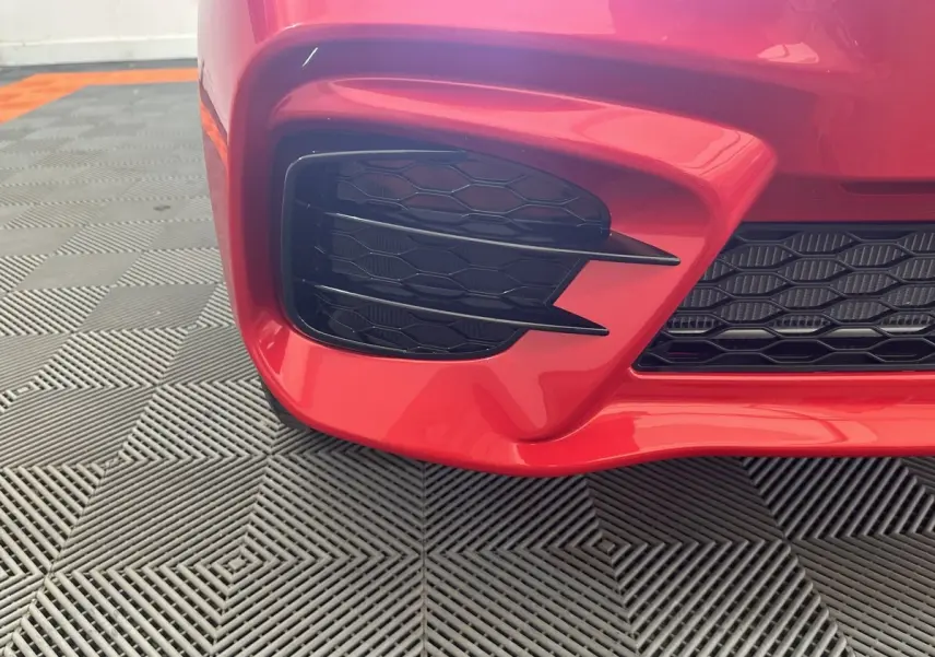 Gros plan sur la partie avant gauche rouge de l'AIXAM AMBITION 0.5 CITY SPORT 2026 avec grille noire à motif nid d'abeille.