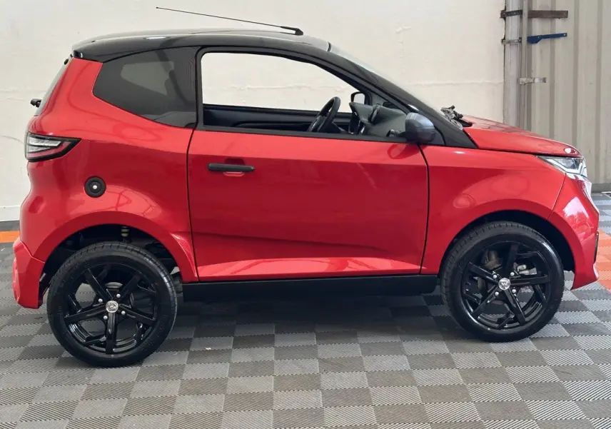 Vue de profil côté gauche d'une Aixam Ambition 0.5 City Sport rouge avec jantes noires et rétroviseur caméra.