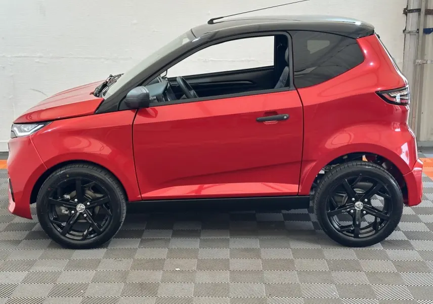 Vue de profil côté gauche d'une Aixam Ambition 0.5 City Sport rouge avec toit noir et jantes noires.