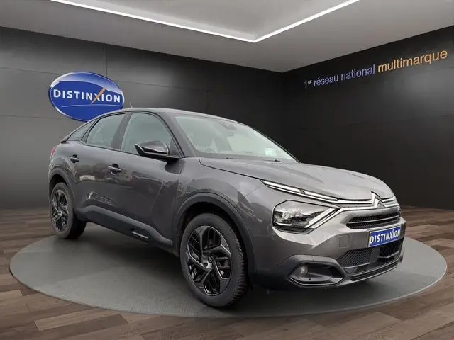 Vue 3/4 avant droite d'une Citroën C4 gris platinium 2022 avec phares LED et jantes noires en showroom.