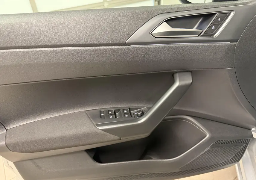 Gros plan sur la porte intérieure côté conducteur du Volkswagen Taigo 2025, avec commandes de vitres et verrouillage en plastique noir.