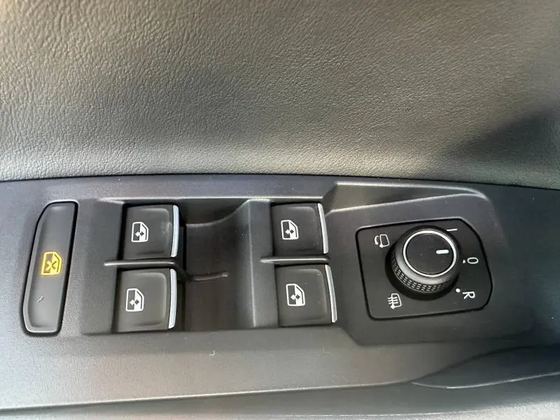 Vue rapprochée des commandes de lève-vitres et rétroviseurs sur la porte côté conducteur d’un Volkswagen T-Cross argenté.