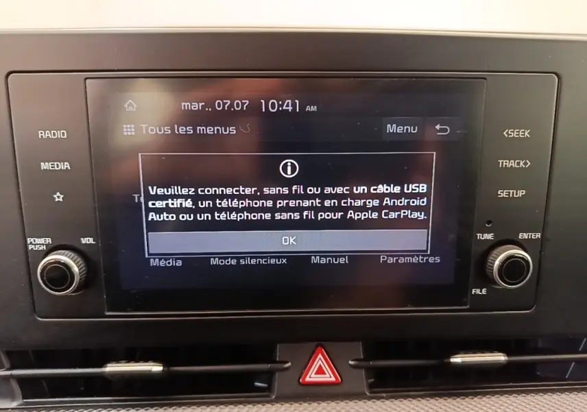 Écran tactile central du tableau de bord du Kia Sportage beige, avec commandes physiques autour et affichage de connexion Apple CarPlay.