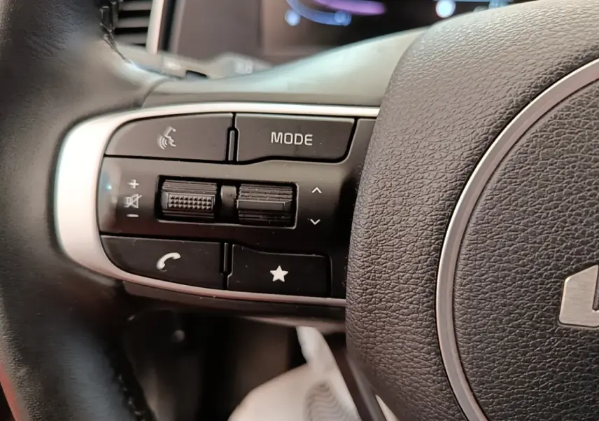 Gros plan sur les commandes du volant cuir noir du Kia Sportage beige, boutons multifonctions visibles.
